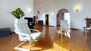 Un'ampia zona giorno con una grande poltrona bianca, una poltrona bianca più piccola e un tavolino rotondo. Sullo sfondo, un'area pranzo con un tavolo e sedie in legno.