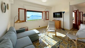 Un soggiorno con divano, poltrone, televisore e vista mare.