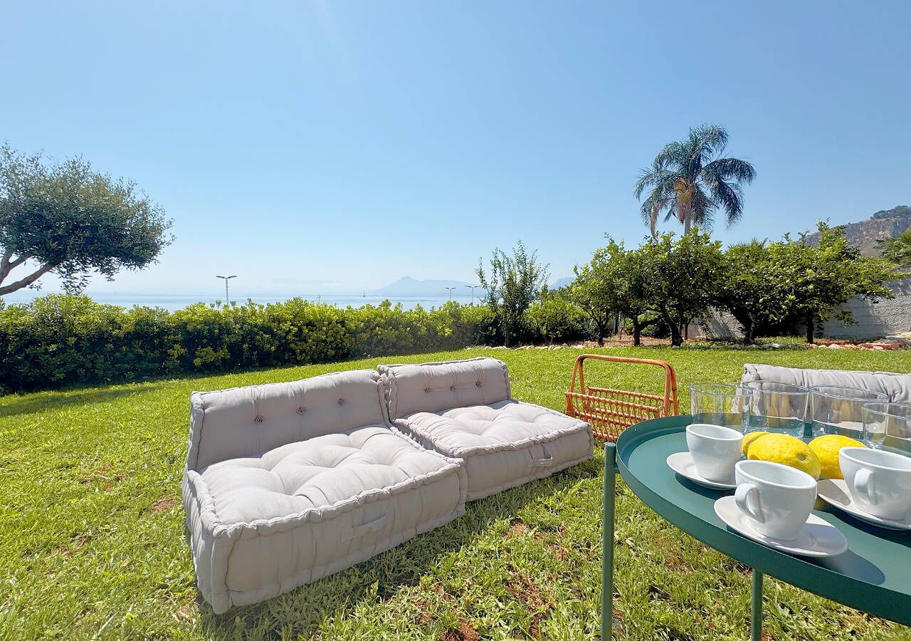 Un espace extérieur verdoyant avec un canapé beige et une table sur laquelle se trouvent des tasses et des citrons.