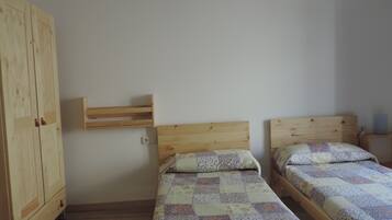 A bedroom with two single beds, wooden headboards, a wooden wardrobe, and a small shelf.