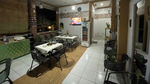 A dining area with a kitchen in the background, featuring a refrigerator, a clock, and a television. - Batukaru Garden 5 Bali Sevilla Residence (Tumbak Bayuh)