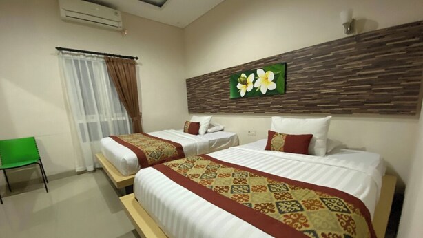 A hotel room with two beds, a green chair, a window with curtains, and a wall-mounted air conditioner. - Batukaru Garden 5 Bali Sevilla Residence (Tumbak Bayuh)
