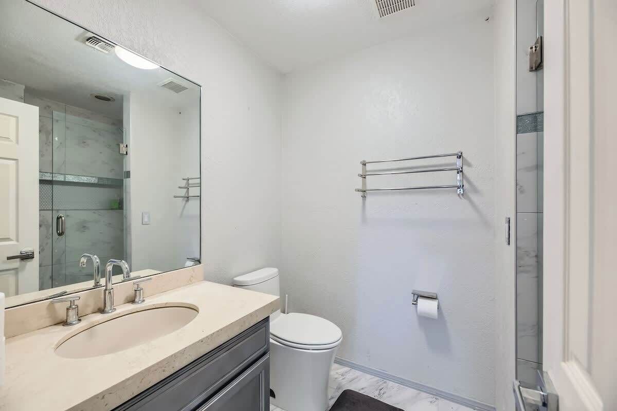 A bathroom with a double sink, a toilet, a shower, and a large mirror.