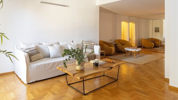 Uma sala de estar moderna com um sofá branco, mesa de centro de madeira e uma planta.