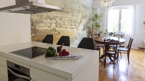 Cozinha moderna com ilha central, área de jantar com mesa redonda e cadeiras, e uma grande janela com luz natural.