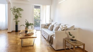 Uma sala de estar com piso de madeira, um sofá branco, uma mesinha e um vaso de planta.