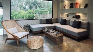 Ein modernes Wohnzimmer mit großem Fenster, einer Couch, einem Sessel und einem Couchtisch.