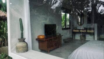 Un dormitorio con un ventanal grande, un aparador de madera, una cama y una planta de cactus.