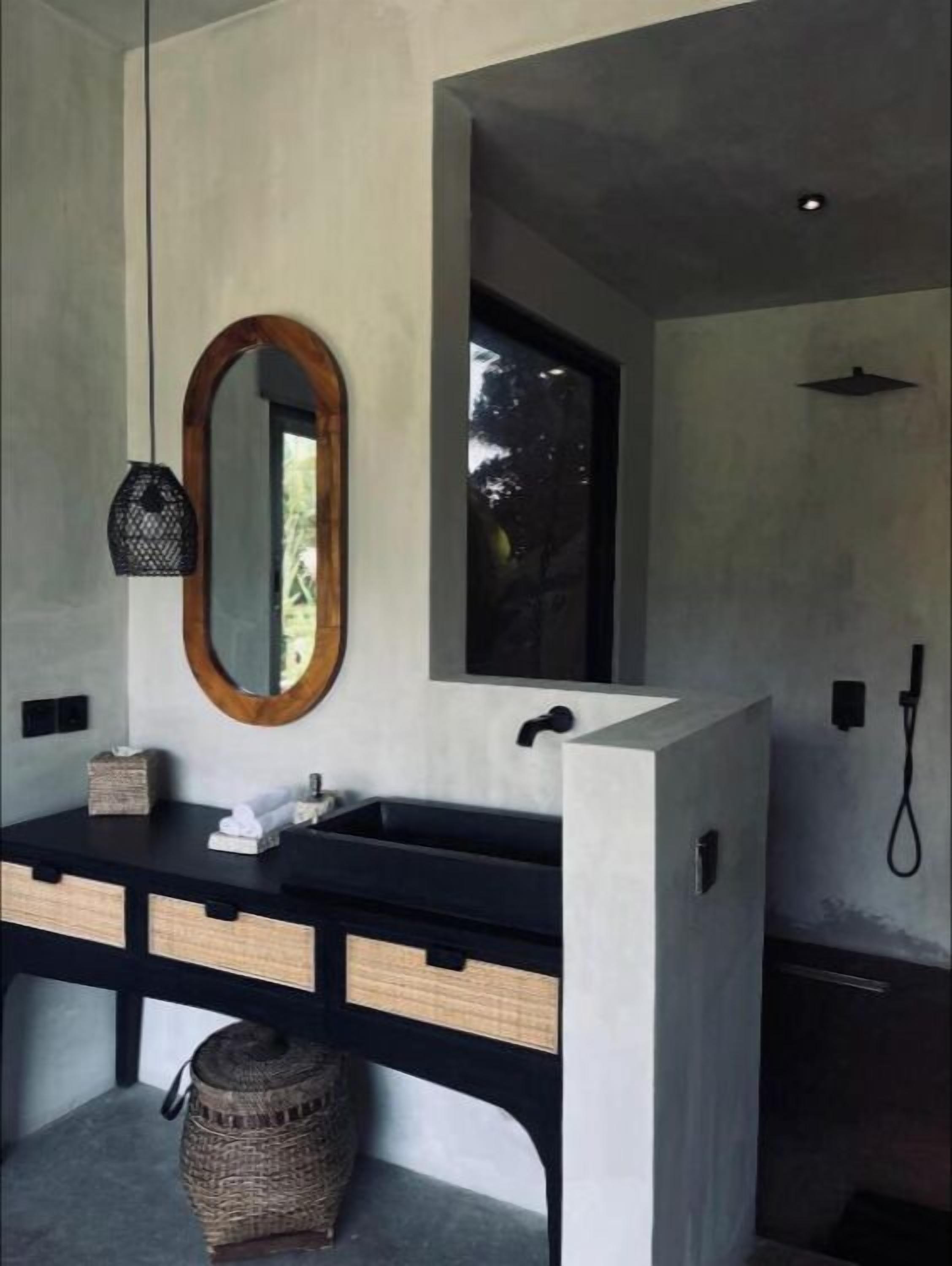 Un baño moderno con tocador negro, espejo con marco de madera y zona de ducha.