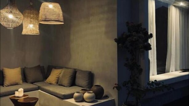 Ein moderner Außenbereich zum Sitzen mit einer Couch, Kissen und einem Tisch, beleuchtet durch Pendelleuchten.