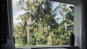 Ein Schlafzimmer mit großem Fenster und Blick auf einen tropischen Garten.
