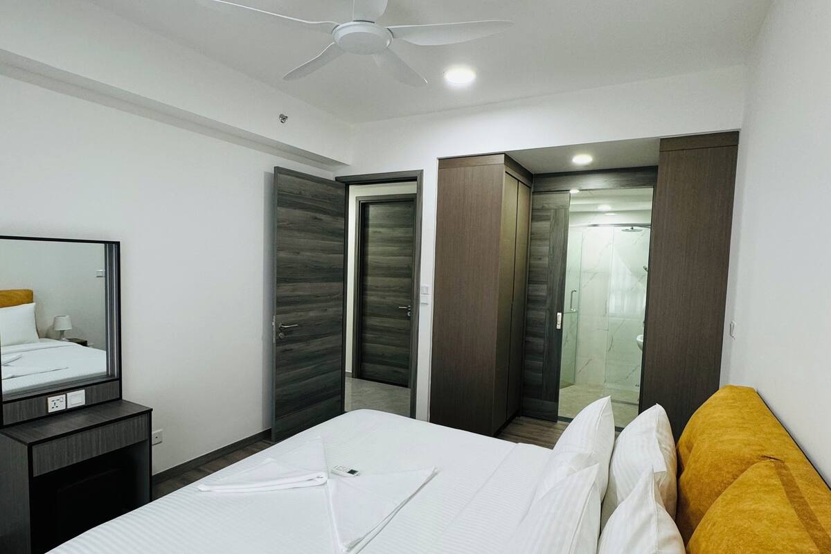 A modern hotel room with a large bed, a bedside table, a mirror, and a ceiling fan.