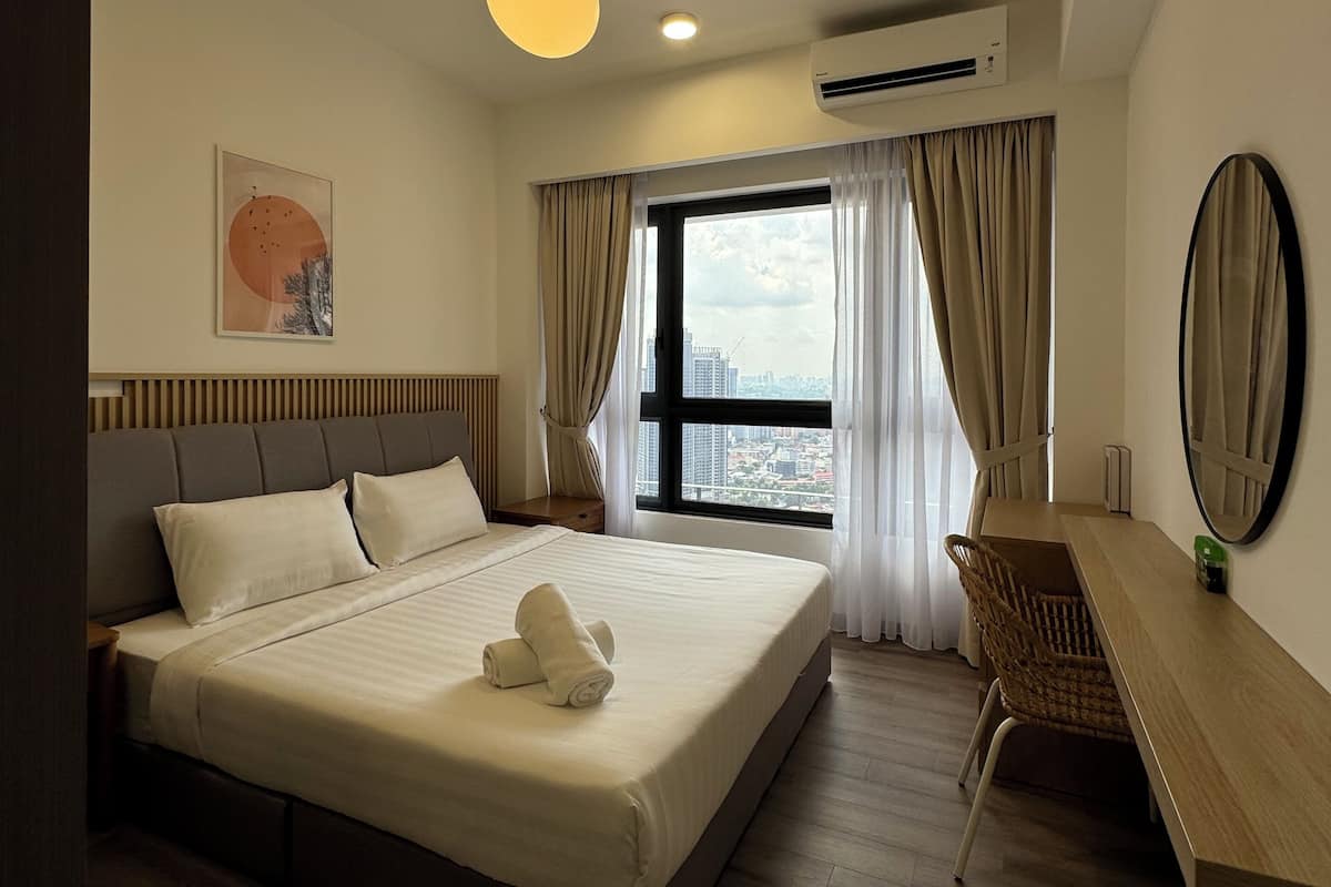 A modern hotel room with a large bed, a desk, and a view of the city through the window.
