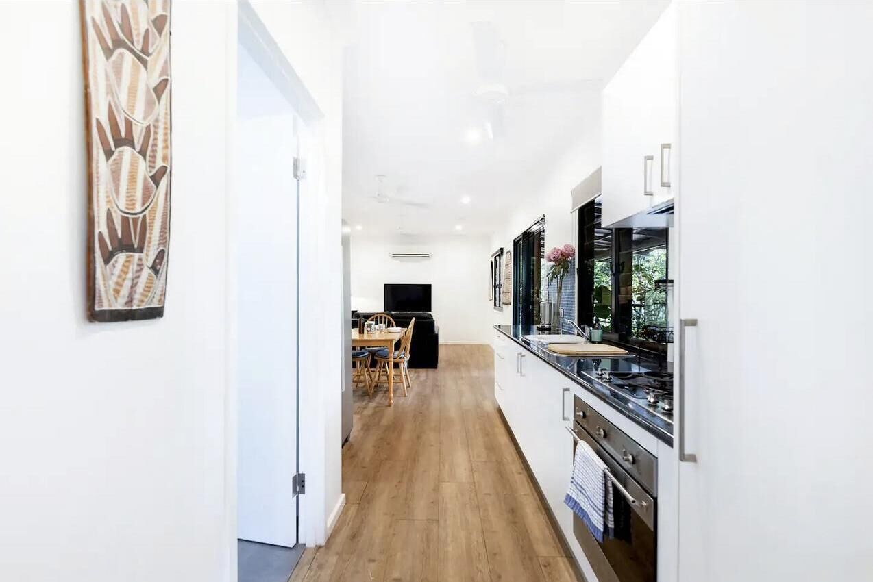 A modern kitchen with white cabinets, a wooden floor, and a dining area with a table and chairs.