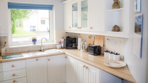 A kitchen with white cabinets, a coffee maker, a kettle, and a toaster. - Dunmore Villas Holiday Home No 1 (Dunmore East)