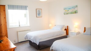 A bedroom with two beds, a window with blinds, a radiator, and a painting on the wall. - Dunmore Villas Holiday Home No 1 (Dunmore East)