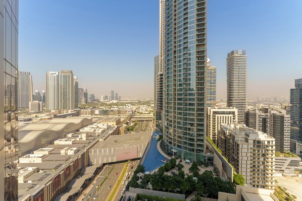 A high-rise building with a curved facade, surrounded by other tall buildings, a road with vehicles, and a small landscaped area with trees.