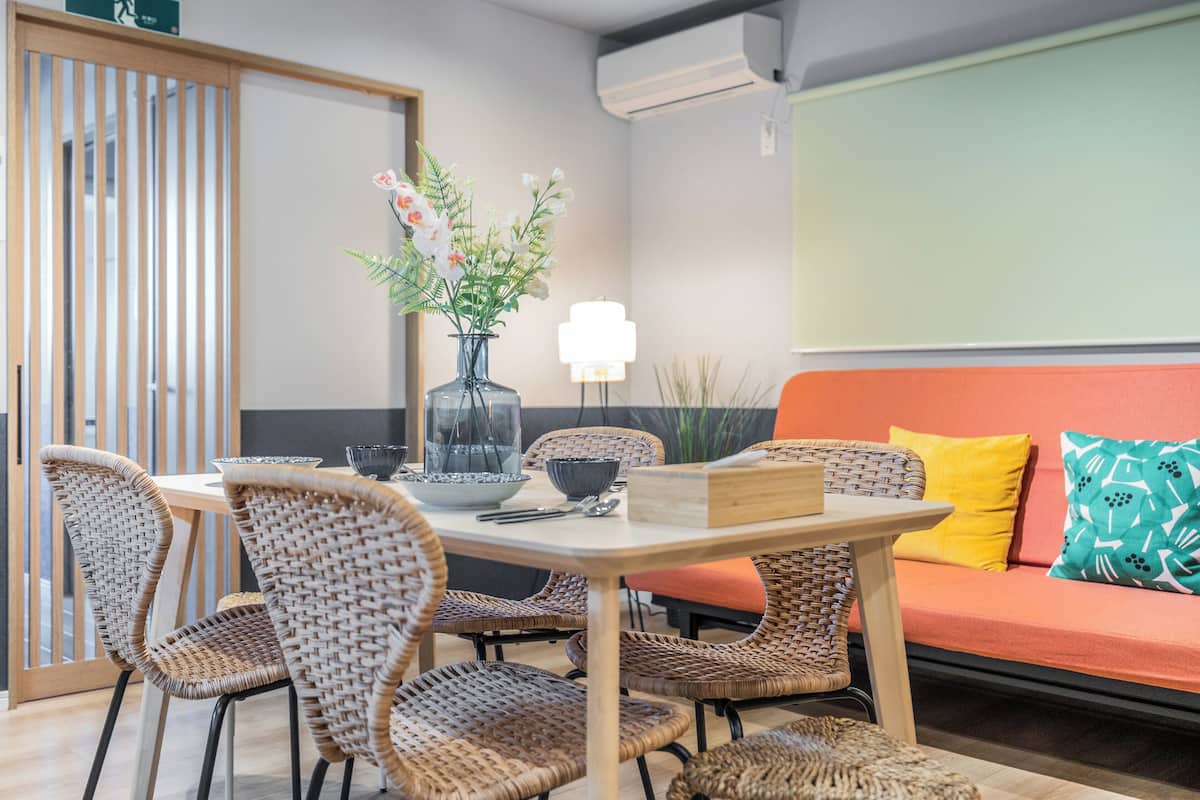 A dining area with wicker chairs, a table with a vase of flowers, and a sofa with colorful cushions.