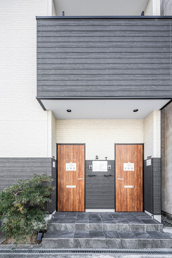 A modern building entrance with two wooden doors, a small plant, and a stone staircase.