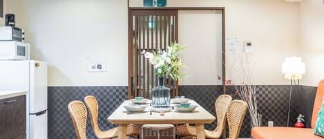Un comedor con una mesa dispuesta para cuatro personas, rodeado de sillas de mimbre, un florero con flores y una puerta de madera al fondo.