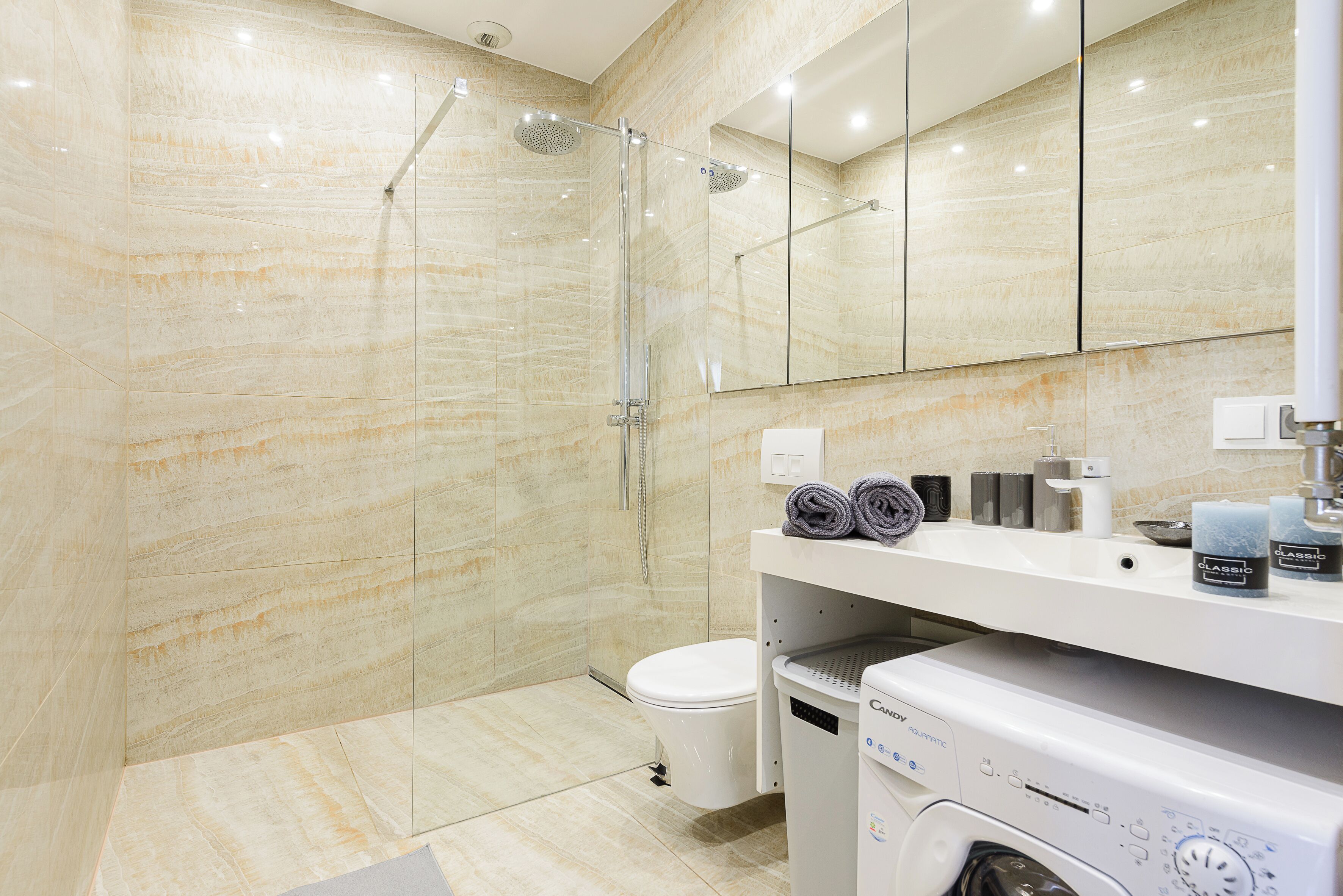 A modern bathroom with a glass-enclosed shower, a toilet, and a washing machine.
