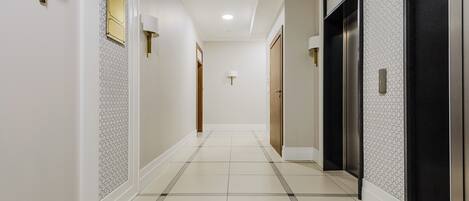 A hallway with a tiled floor, a wall-mounted light fixture, and a door with a handle.