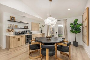 A modern kitchen with wooden cabinets, a round dining table with black chairs, a pendant light, and a large potted plant. - The Palmcroft Resort Oasis| Par2 Golf | 2 Masters (Scottsdale)