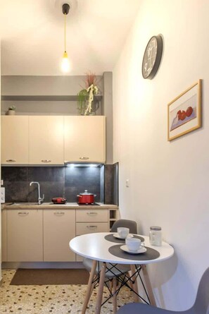 Eine kompakte Küche mit Essbereich, einer Uhr an der Wand und einem kleinen Tisch mit Tassen und einem Krug.