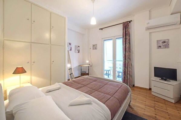 Ein Schlafzimmer mit Bett, Kleiderschrank, Fernseher und einem Balkon mit Vorhängen.