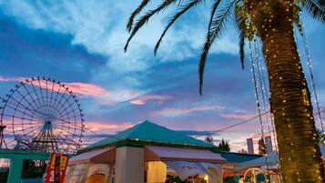A tented food stall with a sign, a palm tree, and a Ferris wheel in the background.