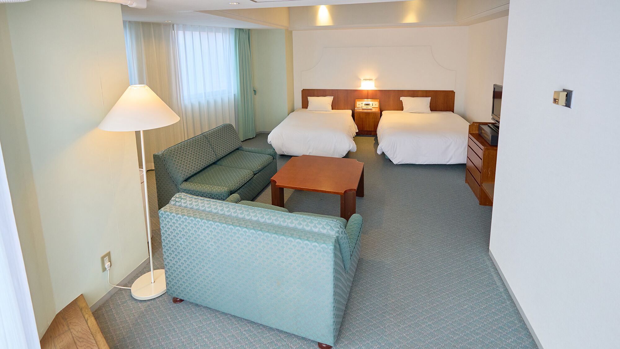A hotel room with two beds, a sofa, a small table, and a lamp.