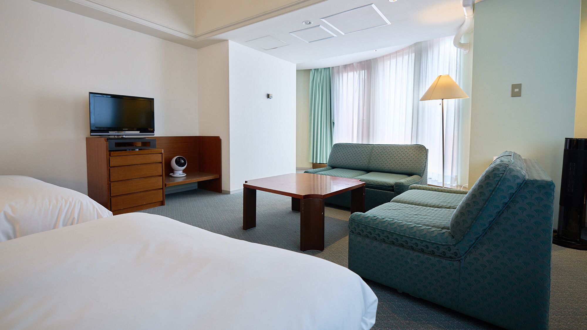 Habitación de hotel con cama, sofá, escritorio, televisor y lámpara.