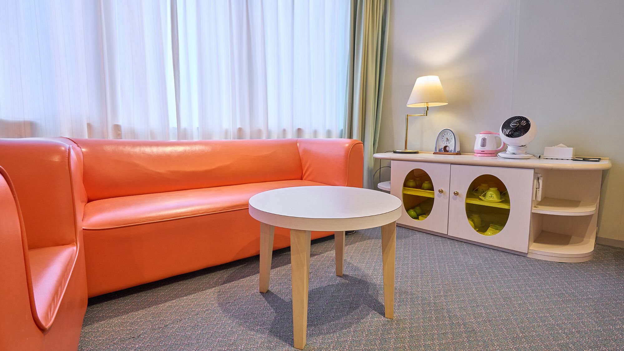 Et værelse med sofa, lille bord, skab med glasdøre, lampe og et ur.