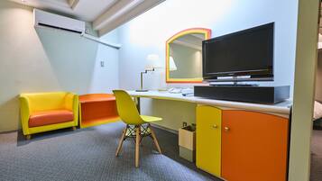 A hotel room with a desk, a chair, a television, a mirror, and a sofa.