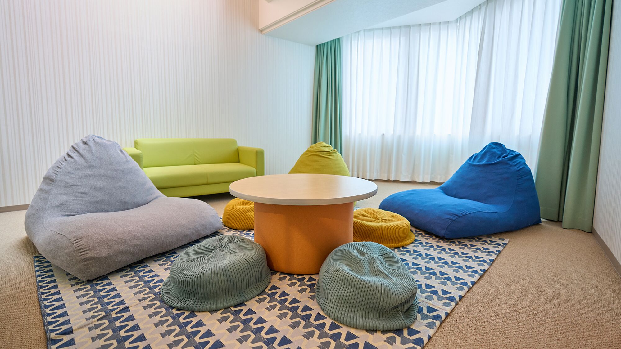 Een kamer met een groene bank, een blauwe krukkop, een ronde tafel en vloermatten met een patroon.