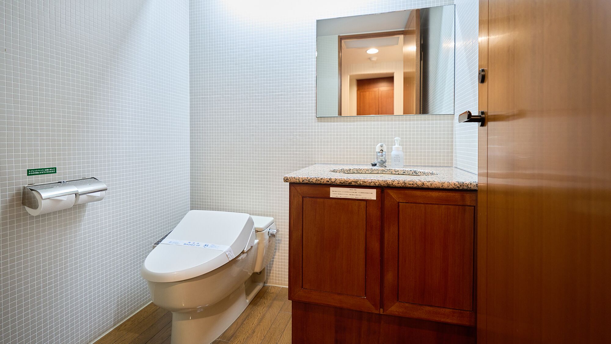 Une salle de bain comprenant des toilettes, un lavabo avec un miroir au-dessus et un porte-rouleau de papier toilette fixé au mur.