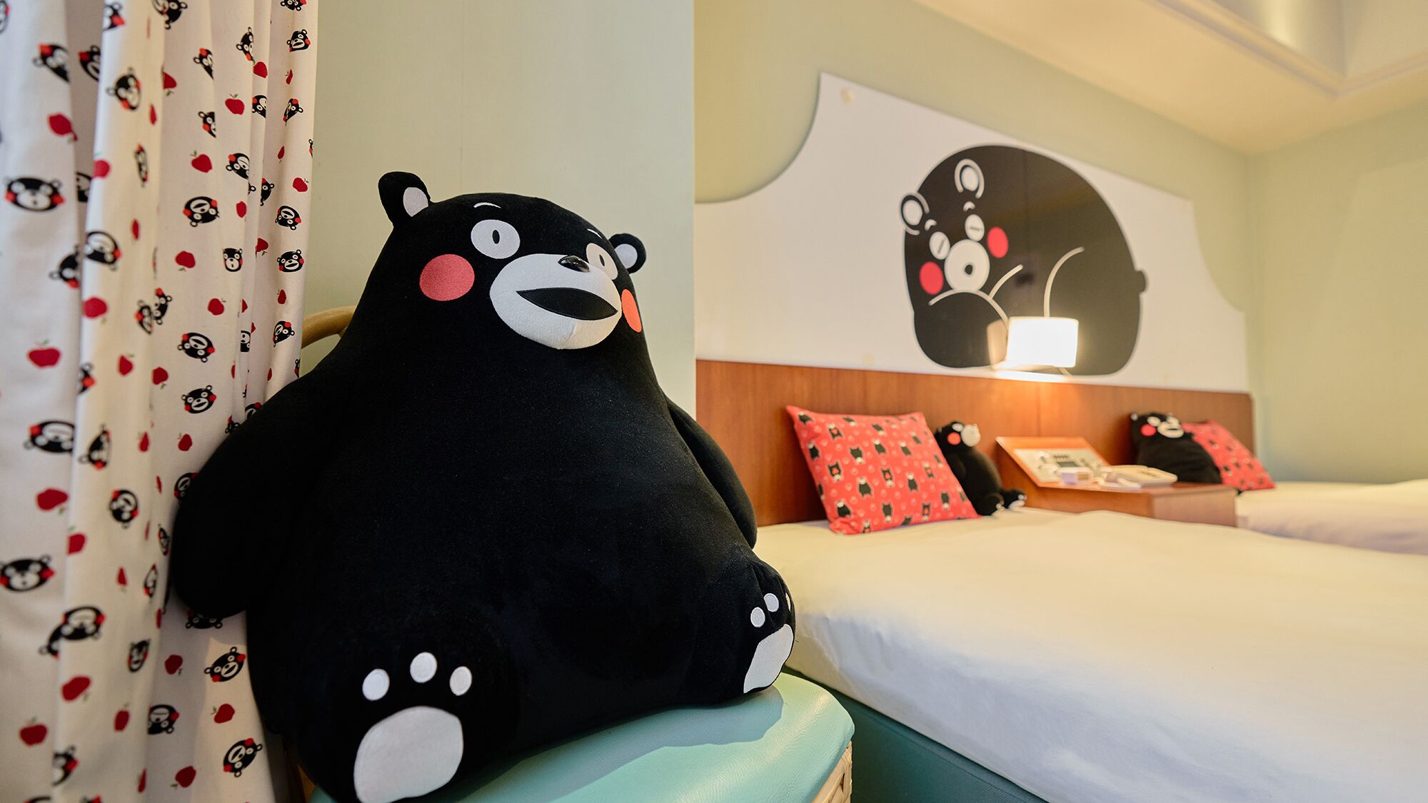 A hotel room with a large black bear plush toy on the bed, a bed with white bedding, a wooden headboard, and a wall with a bear-themed artwork.