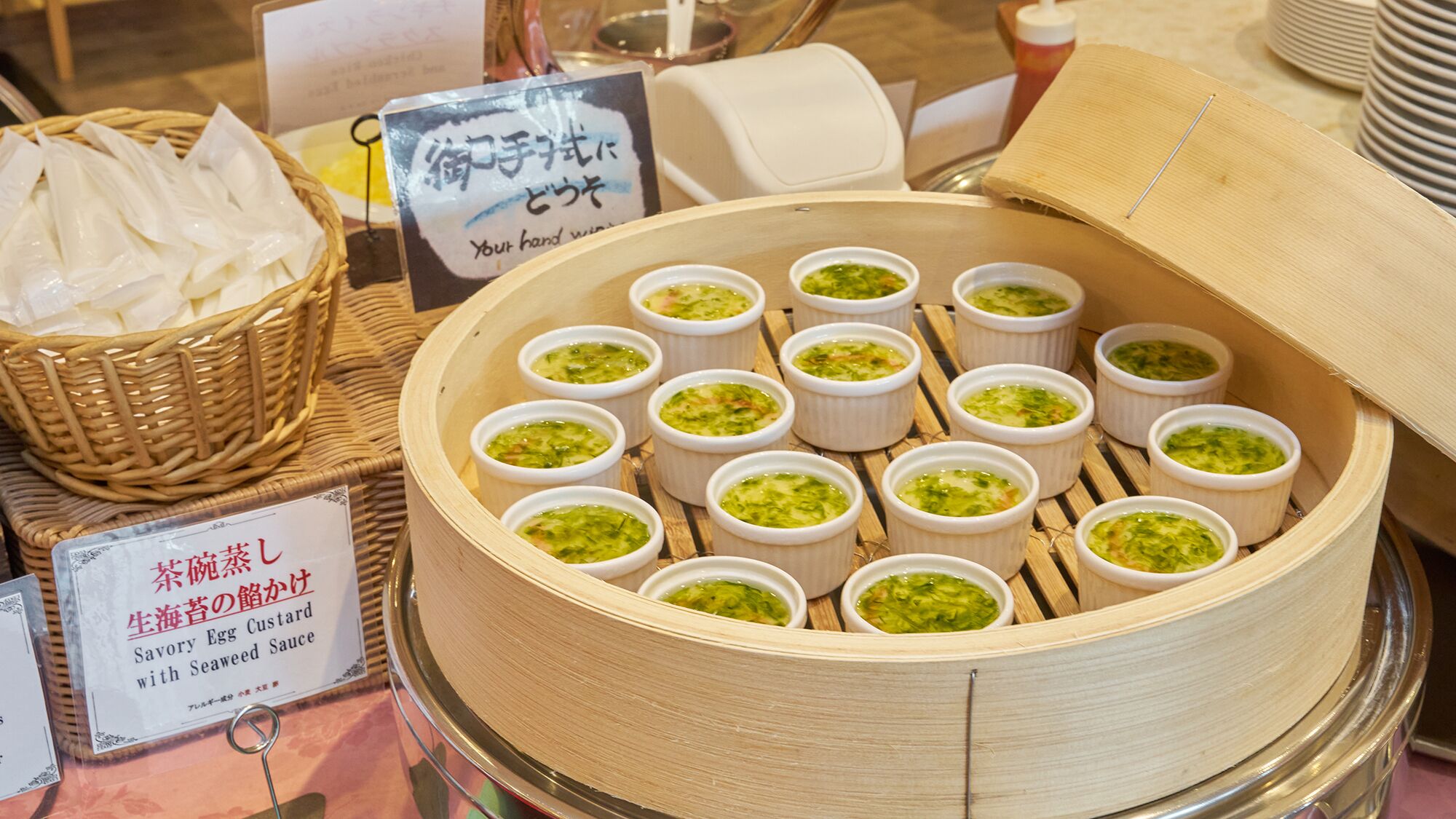 En madpræsentation med flere små skåle grøn creme, et skilt med japansk tekst og en kurv med hvide ting.