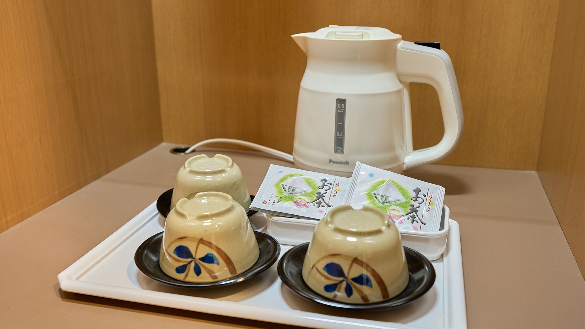 A tray with four ceramic cups and a white electric kettle on a table.