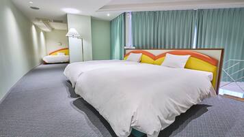 Habitación de hotel con una cama grande, una cama más pequeña, una mesita de noche, una lámpara y vistas al exterior a través de una ventana con cortinas.