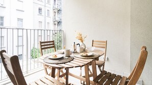 A balcony with a wooden table set for two, chairs, a vase with dried flowers, and a view of a building with multiple windows. - Easylife - Apartment with Terrace and Comfort (Milano)