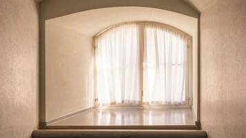 Una habitación con techo curvo, ventana con cortinas de gasa y piso de madera.