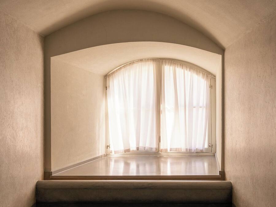 Una habitación con techo curvo, ventana con cortinas de gasa y piso de madera.
