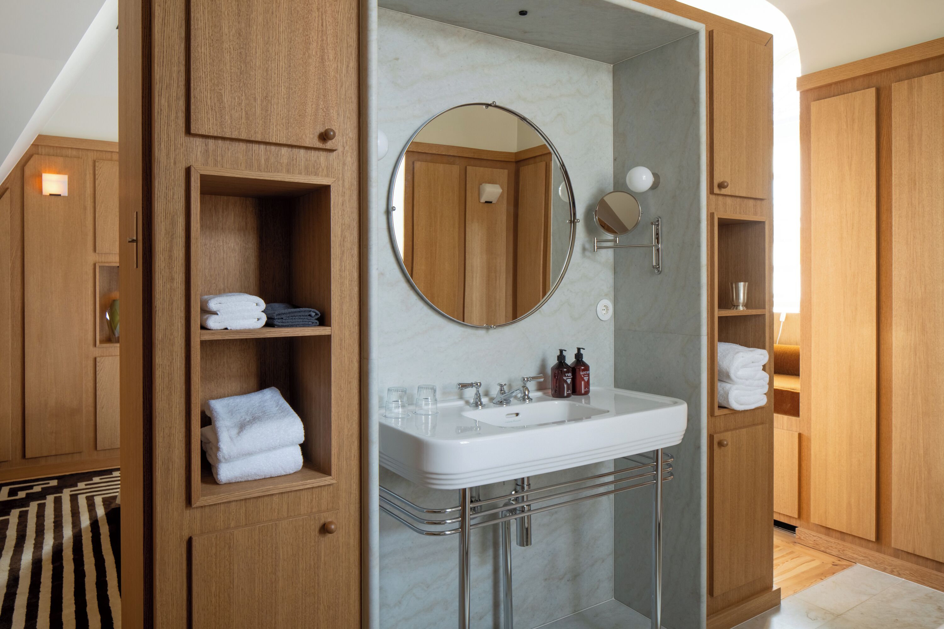 A modern bathroom with a built-in sink, a round mirror, and wooden cabinetry.