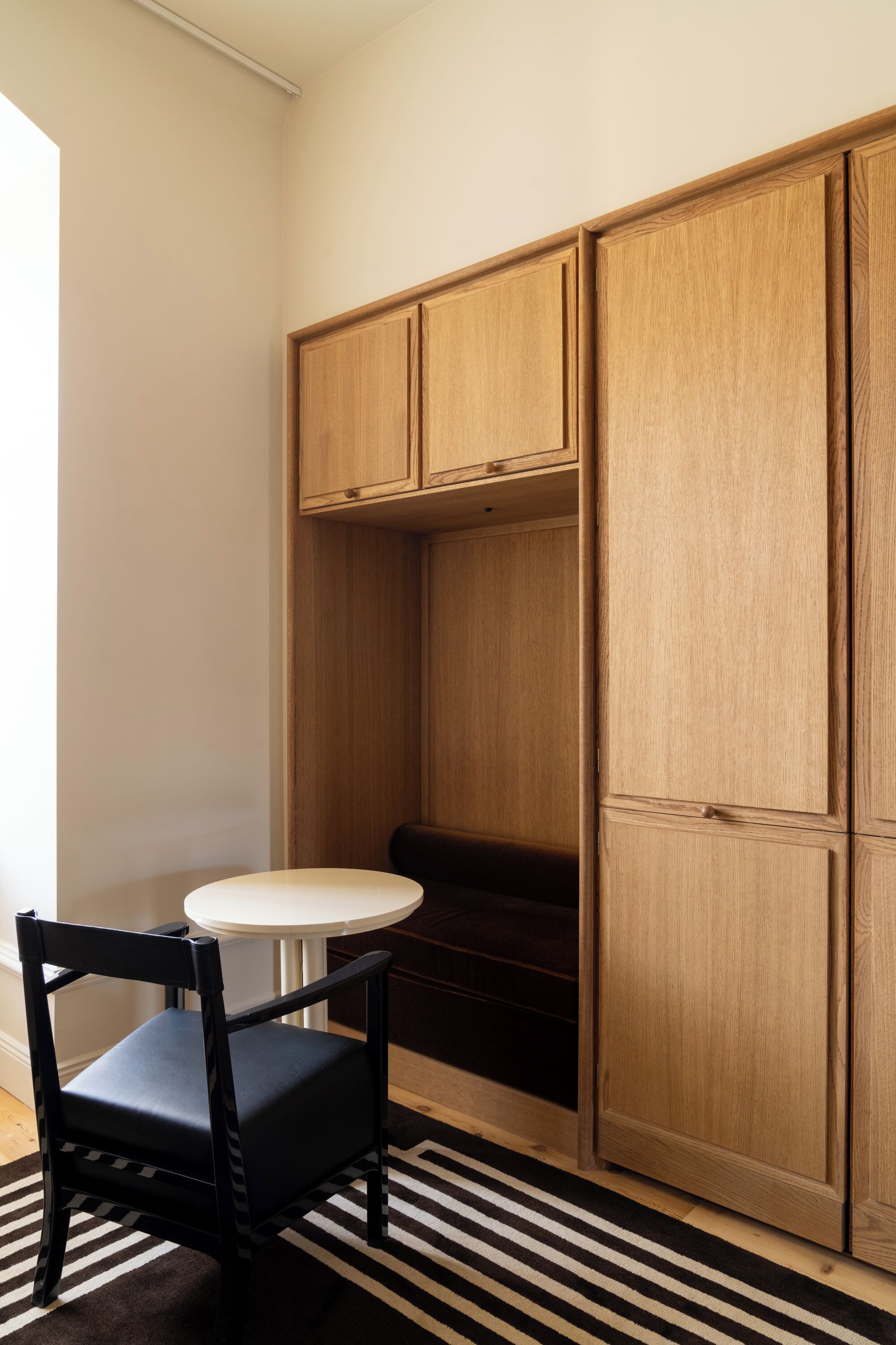 Una habitación con un armario de madera, una silla negra y una mesa blanca.
