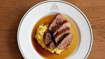 Een bord eten met een witte rand en zwarte rand, met plakjes vlees en aardappelpuree met bruine saus.
