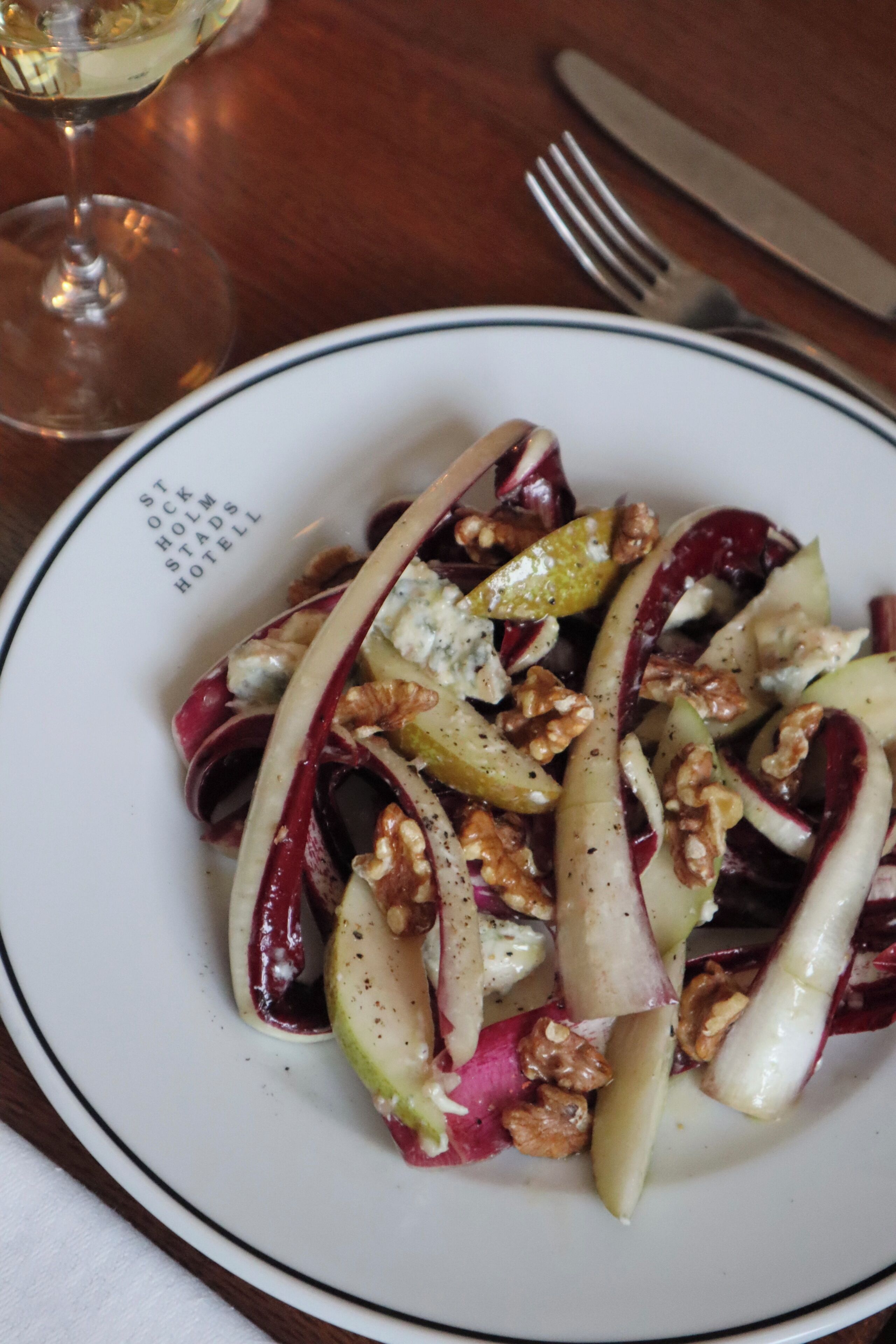 Un plato de comida con nueces y fruta, un tenedor y un cuchillo sobre una mesa.