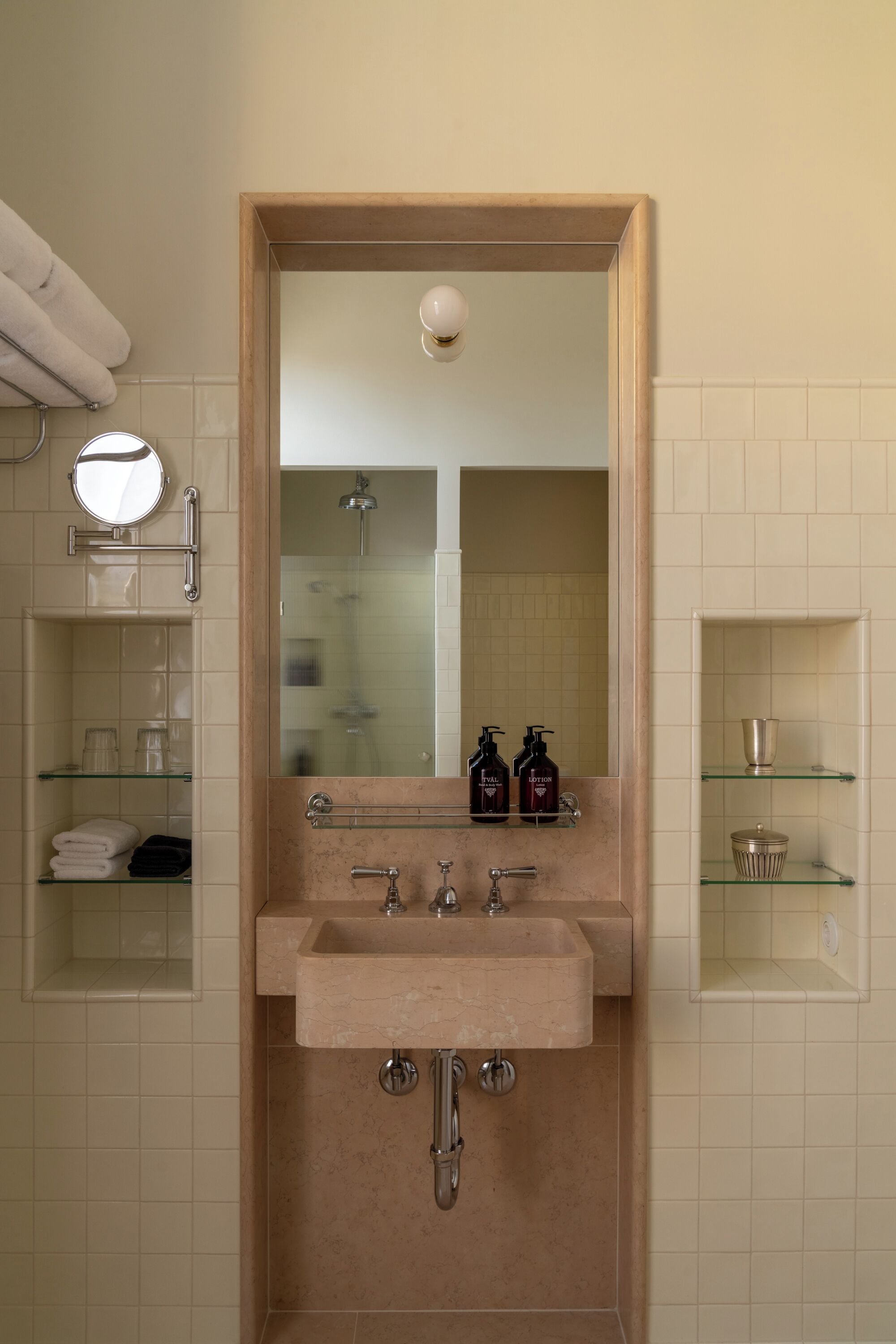 A bathroom with a sink, mirror, and glass shelves.