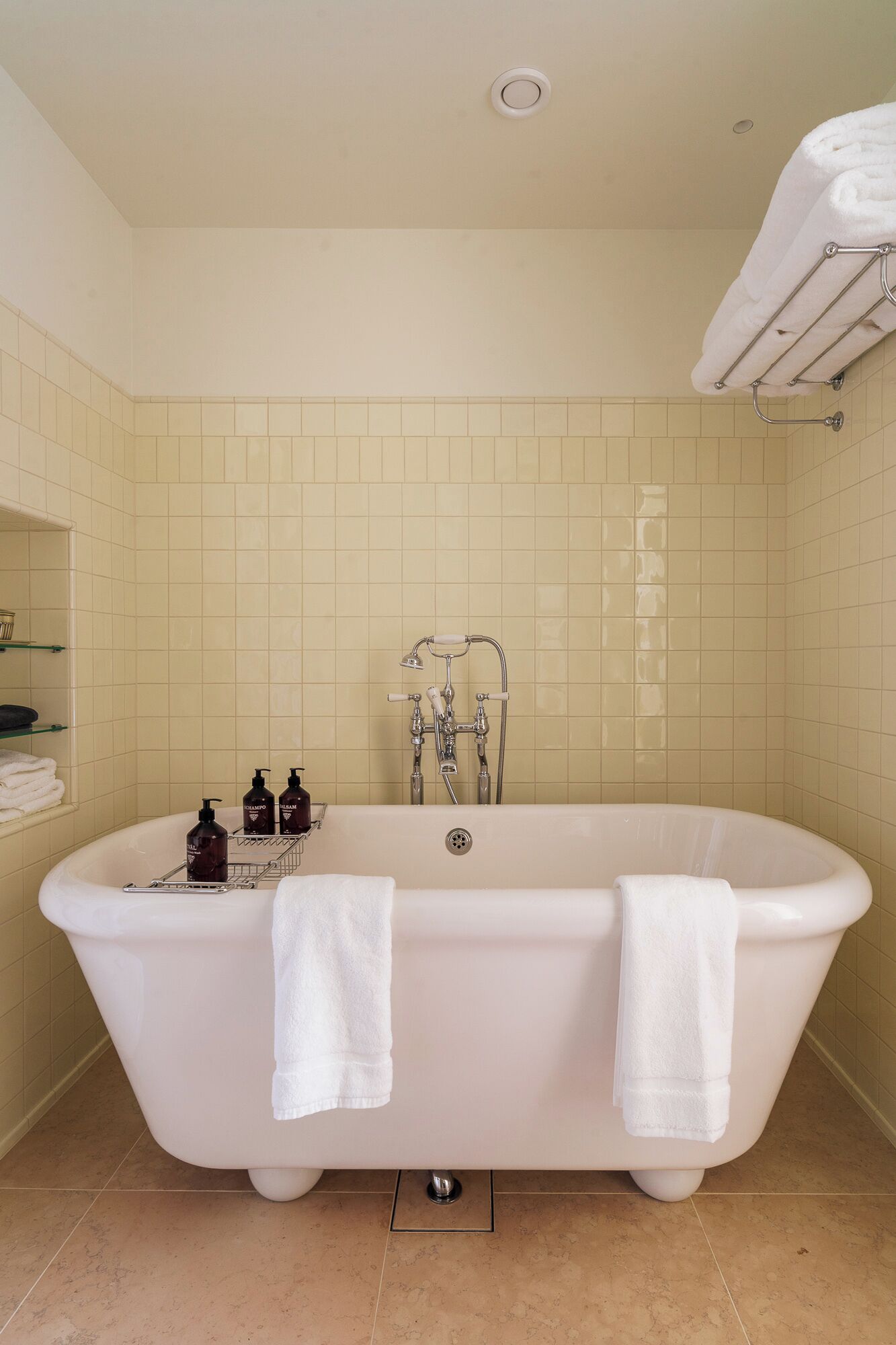 A bathroom with a freestanding bathtub, two towels, a showerhead, and toiletries on a shelf.