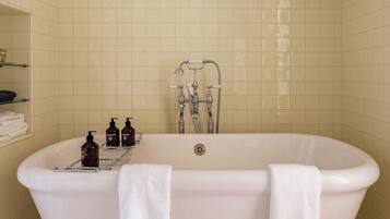 A bathroom with a freestanding bathtub, two towels, a showerhead, and toiletries on a shelf.